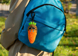 Blue backpack with a carrot-shaped keychain featuring sunglasses and a hat, outdoors.